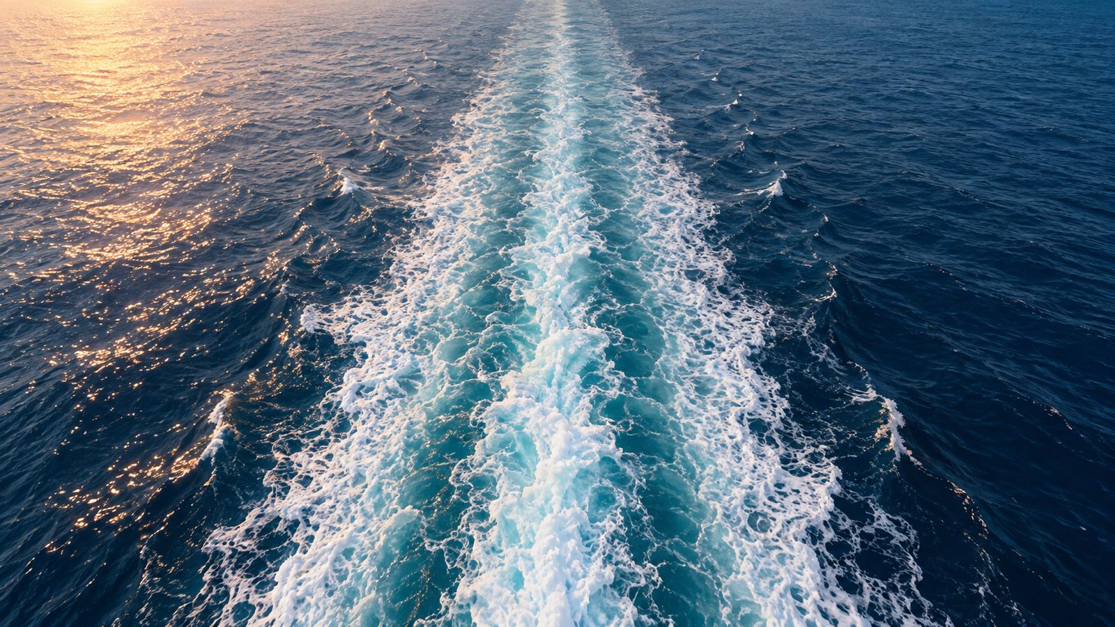 The white wake of a ship stretching across a deep blue ocean in evening light