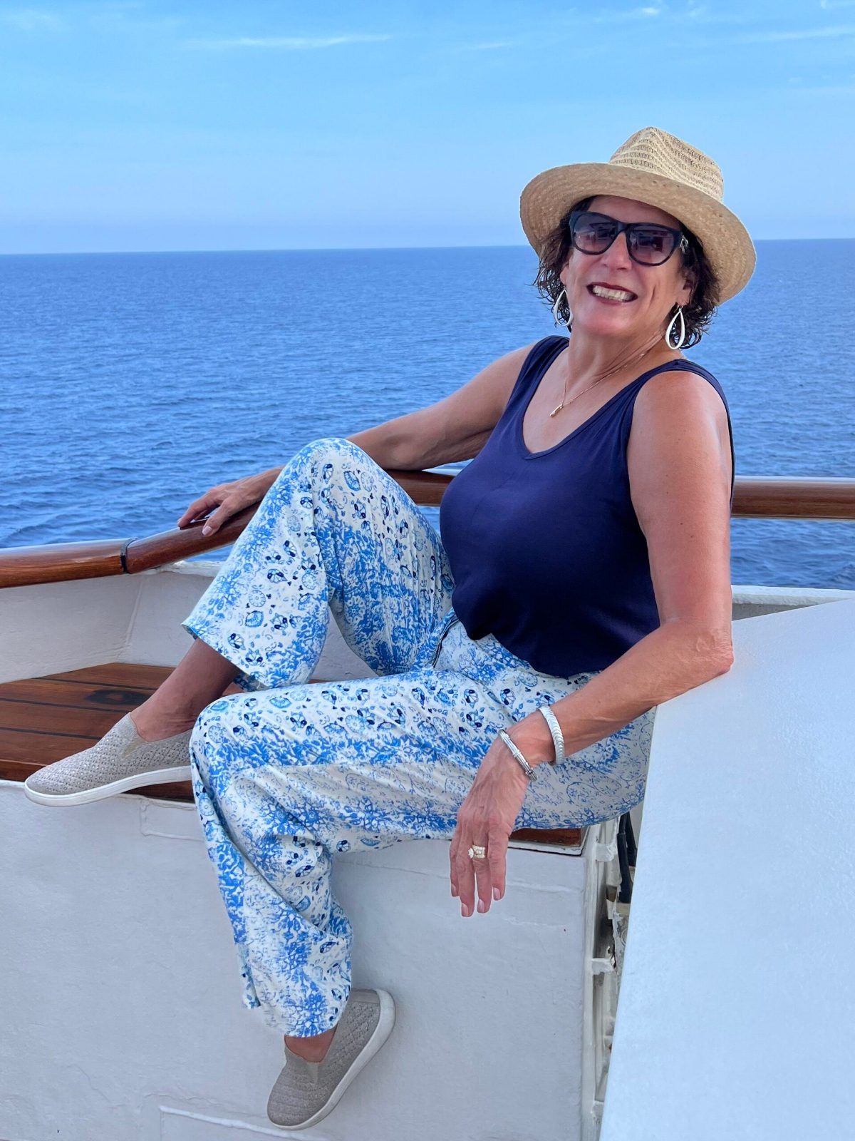 Joanne Mitchell of My Best Cruise Gal smiling on the deck of a cruise ship, in a straw hat, with the open sea behind her